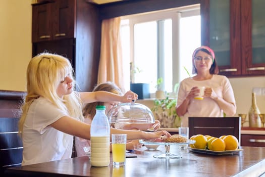 Children two sisters eating at home in the kitchen, teenage and preteen girls having breakfast together, mother cooking. Family, people, children, food, lifestyle concept