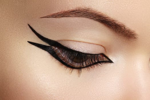 Beautiful macro shot of female eye with classic eyeliner makeup. Perfect shape of eyebrows, brown eyeshadows and long eyelashes. Cosmetics and make-up. Closeup macro shot of fashion liner eyes visage