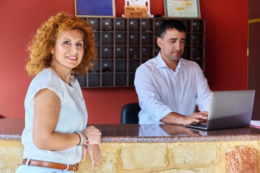 Small resort staff at reception. Portrait of a middle-aged female hotel owner. Small business, booking, tourism, work concept