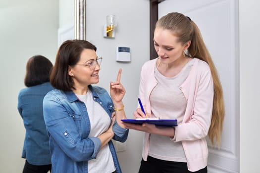 Female social worker talking to middle aged woman at home near front door. Social services, survey, help concept