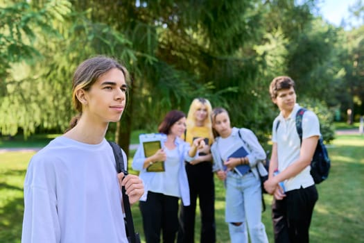Male student 16, 17 years old with backpack, group of teenagers talking with teacher in school park. Back to school, back to college, high school, education, adolescence, teenage students concept