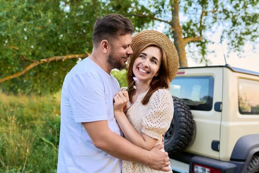 Love and romance of middle-aged couple. Happy hugging man and woman near car, summer nature wild meadow background. Relationship, holiday, date, trip, journey, weekend, family, people 40s concept