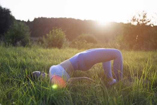 girl of fair appearance with tied hair,dressed in blue clothes for phineas,does yoga outdoors at sunset.healthy lifestyle concept,there is a place for an inscription. High quality photo