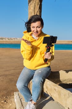 Mature woman recording video on a smartphone, journalist blogger making a stream, on the seashore. Freelance, blogging, lifestyle, technology concept