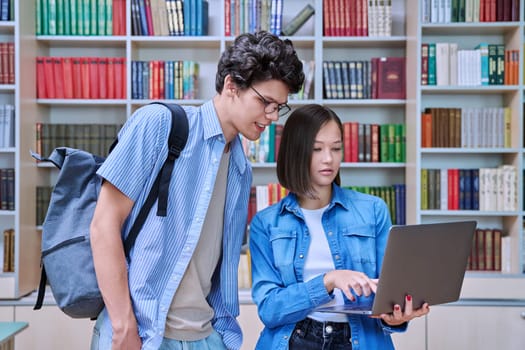 Young students male and female in college library talking, studying, preparing for exams, with laptop. Knowledge, education, youth, college university concept