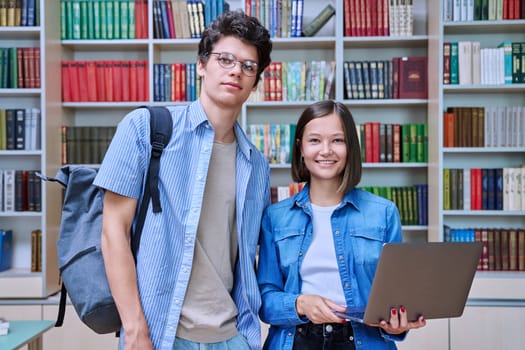 Portrait of two college students, guy and girl, smiling looking at camera inside library. Knowledge, education, youth, college university concept