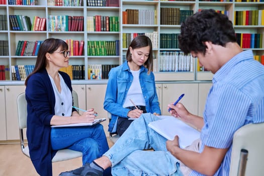 College students discussing their studies with female teacher mentor inside library in educational building. Counselor psychologist social worker at group therapy with students, mental health concept