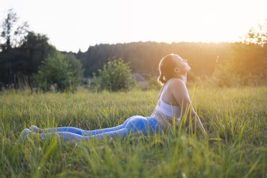 girl of light, athletic appearance, in blue leggings and a white topic goes in for sports in the park on the grass. The concept of a healthy lifestyle, a photo angle from the side. High quality photo