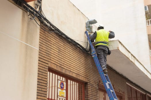 a man in work clothes, turned with his back to the camera, makes wiring on a stepladder. There is a place for an inscription. High quality photo