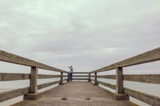 two girls are standing in jackets on a bridge in the distance and taking pictures on the phone, there is a place for an inscription beautiful sea landscape. High quality photo