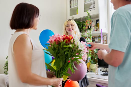 Parents congratulating teenage daughter with happy birthday, gift flowers balloons, children's room interior. Dad and mom with surprise gift. Family, relationship, adolescent concept
