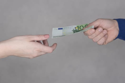 hands giving money 100 euro isolated on gray background close-up.Finance concept.male hand in a blue sweater gives 100 euro to female hands on a gray background. High quality photo