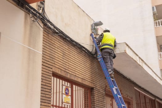 A man in a reflective vest stands on a stepladder doing electrics. A man in work clothes repairs the cable at home. High quality photo