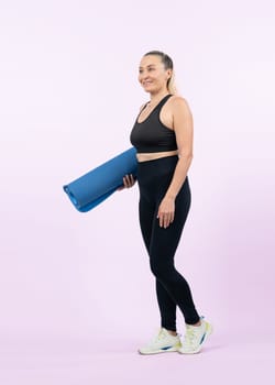 Full body length shot athletic and sporty senior woman holding fitness exercising mat on isolated background. Healthy active physique and body care lifestyle after retirement. Clout