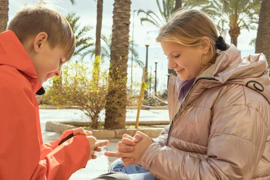 smiling children sit in the park on a bench in jackets play games, brother and sister play in the park. High quality photo