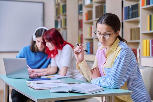 High school students studying in library class, teenage girl in focus. Group of teenagers sitting at desk, writing in notebooks, using laptop books. Knowledge, education, adolescence concept