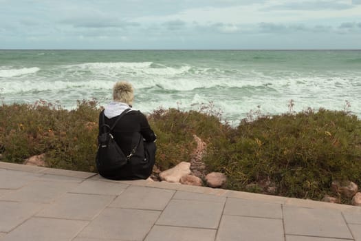 The girl sits on the embankment and looks at the sea. the girl sits with her back to the camera. High quality photo