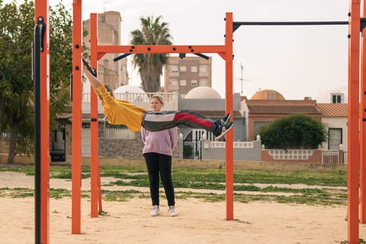 boy and a girl are teenagers on the playground in the park go in for sports. The boy pulls himself up on the horizontal bar, the girl stands nearby. Healthy lifestyle of teenagers. High quality photo