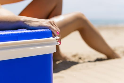 tanned female legs close-up, on the beach and next to it stands a blue portable refrigerator for drinks. The concept of summer holidays on the beach. High quality photo