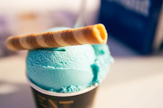 a ball of ice cream in a paper cup on top with a tube of sweet, a close-up on the ice cream that stands on the table there is a place for an inscription. High quality photo