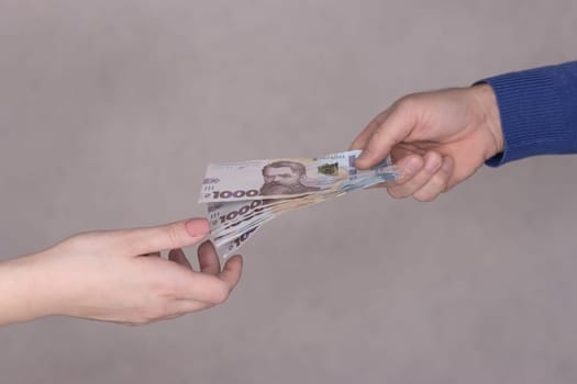 hands giving money isolated on gray background.Finance concept.A man in a blue waiter gives a stack of money of 1000 hryvnia to a woman's hands on a gray background. High quality photo