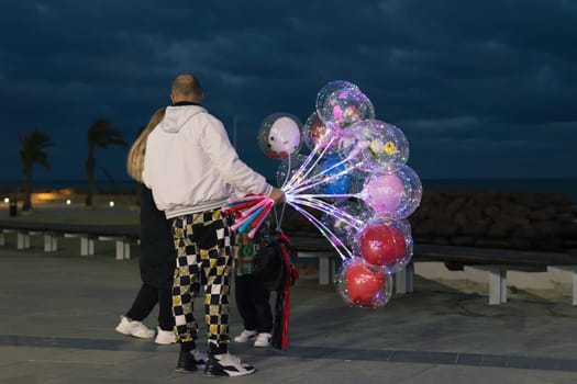 the guy stands with his back to the camera and holds in his hand a lot of multi-colored balloons of different colors and wants to give them to the girls on the waterfront. High quality photo