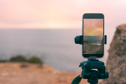 has a place for an inscription close-up on the phone,smartphone camera stands on a tripod close-up, photographing a picturesque evening sunset over a tropical sea and a mountain. High quality photo