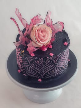 frosted icing black decorate cake for birthday celebration, real rose topping and pink sweet swirls studio isolated shot