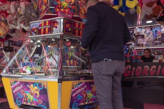 amusement park in the city, a machine for playing with coins, a man stands with his back to the camera, plays the machine, wants to win a toy, gambling. High quality photo