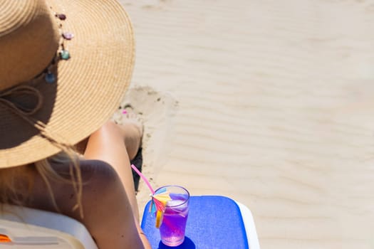 A woman in a bathing suit and a hat sits in a sun lounger with a glass of cocktail back view, a beautiful seascape has a place for an inscription. High quality photo