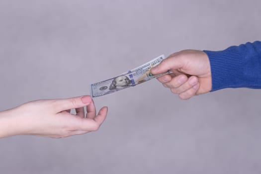 hands giving money 100 dollars isolated on gray background.Finance concept.male hand in a blue sweater gives 100 dollars to female hands on a gray background. High quality photo