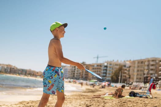 happy child of European appearance on the beach walks in tennis, the boy is standing in swimming trunks and in a green cap on the beach, a happy child is resting on the sea. High quality photo