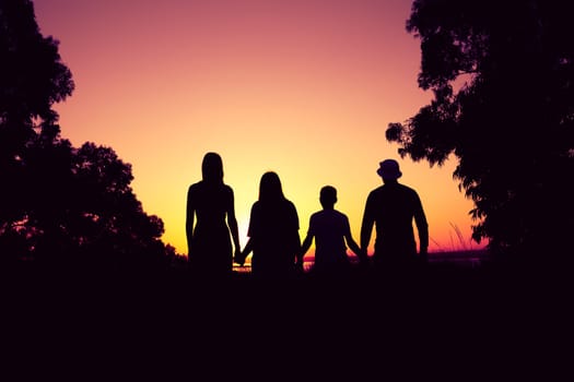 silhouette of a family including father, mother and two children all holding hands against the backdrop of nature and sunset. concept of family and support. High quality photo