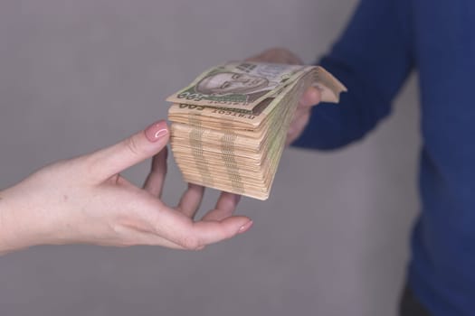 hands giving money isolated on a gray background.Finance concept.A man in a blue waiter gives a stack of money of 500 hryvnia to a woman's hands on a gray background. High quality photo