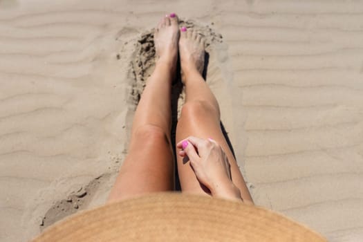 tanned sexy girl is sitting on the beach in a bikini in a brown hat, side view, there is a place for an inscription. High quality photo