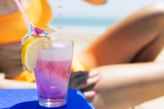 a pink cocktail close-up on the beach, a girl in a swimsuit lies on a sun lounger next to it stands a close-up of a pink color cocktail. The concept of relaxing on the beach. High quality photo