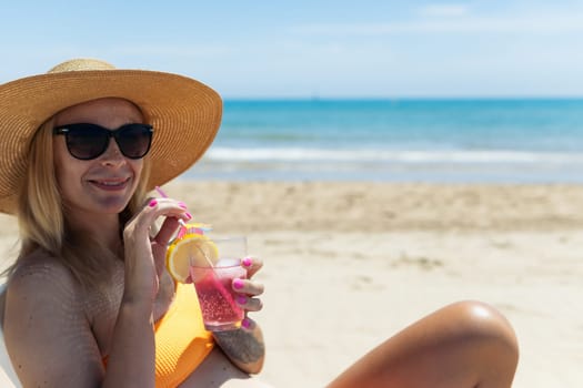 A sexy blonde in a bright bikini is sunbathing on a sun lounger with a cocktail in her hand by the sea. there is a place for an inscription. High quality photo