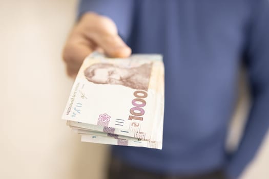 A man in a blue sweater holds a stack of new banknotes of the Ukrainian hryvnia in his hands 1000 hryvnia.On a light background.1000 hryvnia. High quality photo.Finance concept