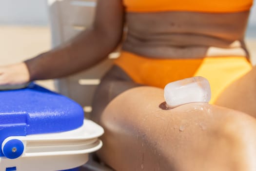 a girl in a bathing suit sits on the beach, takes out ice from a portable refrigerator. summer photo. High quality photo