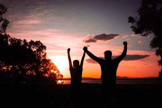 silhouette of father and son against nature background with raised hands, concept of family and success, close-up with space for inscription. High quality photo