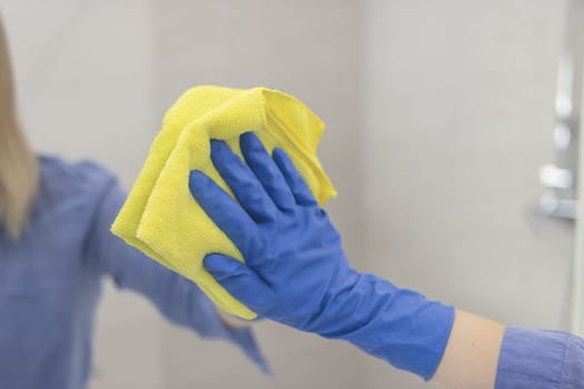 happy blond girl with European appearance washing mirror with yellow cloth in blue gloves at home.House cleaning concept
