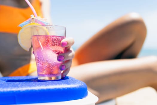 a sexy girl takes a pink cocktail close-up on the beach, a girl in a swimsuit lies on a sun lounger near the pool, close-up.The concept of relaxing on the beach. High quality photo