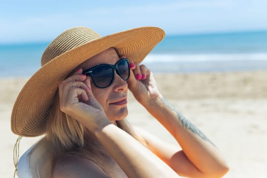 portrait of a beautiful tanned girl in sun glasses and a hat sitting on the beach, there is a place for an inscription. High quality photo