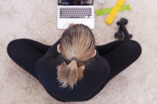 Athletic young girl of European nationality sits and rests after training at home online on the floor. The concept of relaxation and home workout.