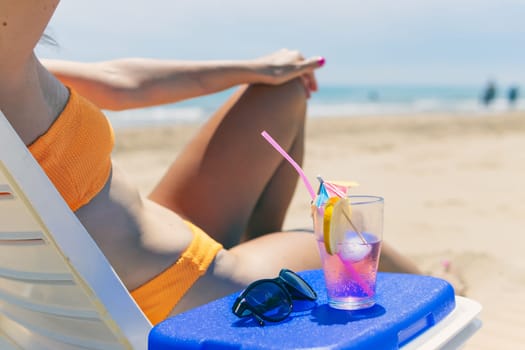 a sexy girl takes a pink cocktail close-up on the beach, a girl in a swimsuit lies on a sun lounger near the pool, close-up.The concept of relaxing on the beach. High quality photo