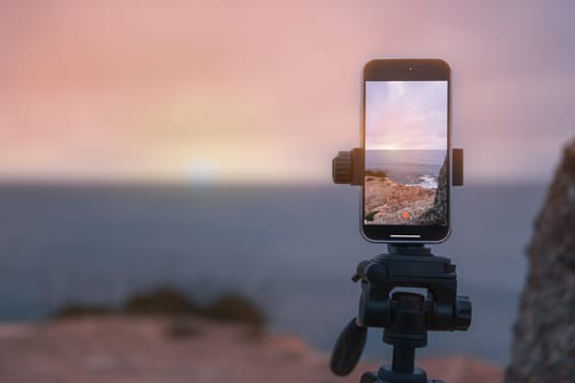 the phone on a tripod stands at dawn on a mountain by the sea and photographs the dawn. A beautiful seascape has a place for an inscription close-up on the phone. High quality photo