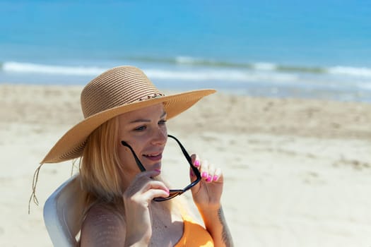 portrait of a beautiful tanned girl in sun glasses and a hat sitting on the beach, there is a place for an inscription. High quality photo