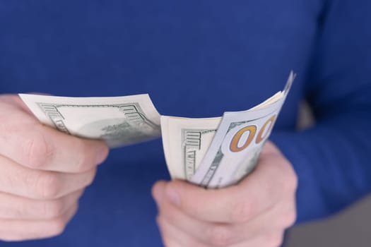 A man in a blue jumper holds a stack of 100 dollars in his hands close-up and counts them.Money concept. High quality photo