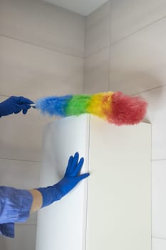 A girl in blue gloves and a blue shirt cleans the dust in the bathroom with a colored napkin, housekeeping concept