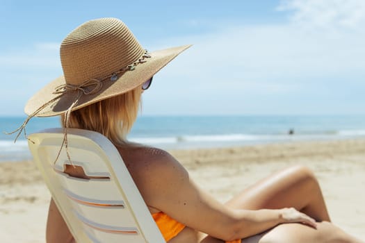 tanned sexy girl is sitting on the beach in a bikini in a brown hat, side view, there is a place for an inscription. High quality photo